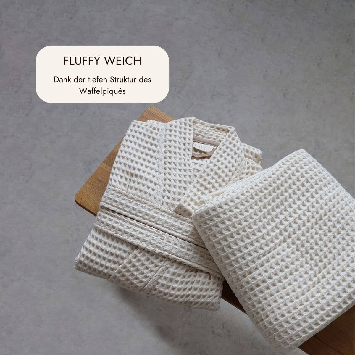Gefalteter Bademantel und Saunatuch aus fluffig weichem Waffelpiqué in Natur auf einem Holzhocker