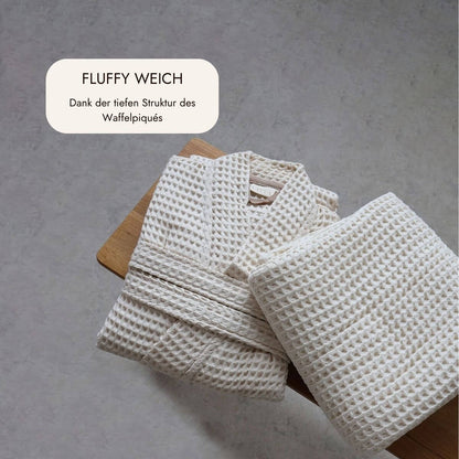 Gefalteter Bademantel und Saunatuch aus fluffig weichem Waffelpiqué in Natur auf einem Holzhocker