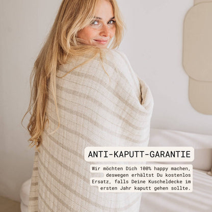 Kuscheldecke (135x200 cm) aus 70% Leinen und 30% OEKO-TEX zertifizierter Baumwolle | Kuscheldecke in der Farbe Beige | Frau steht in Decke eingewickelt
